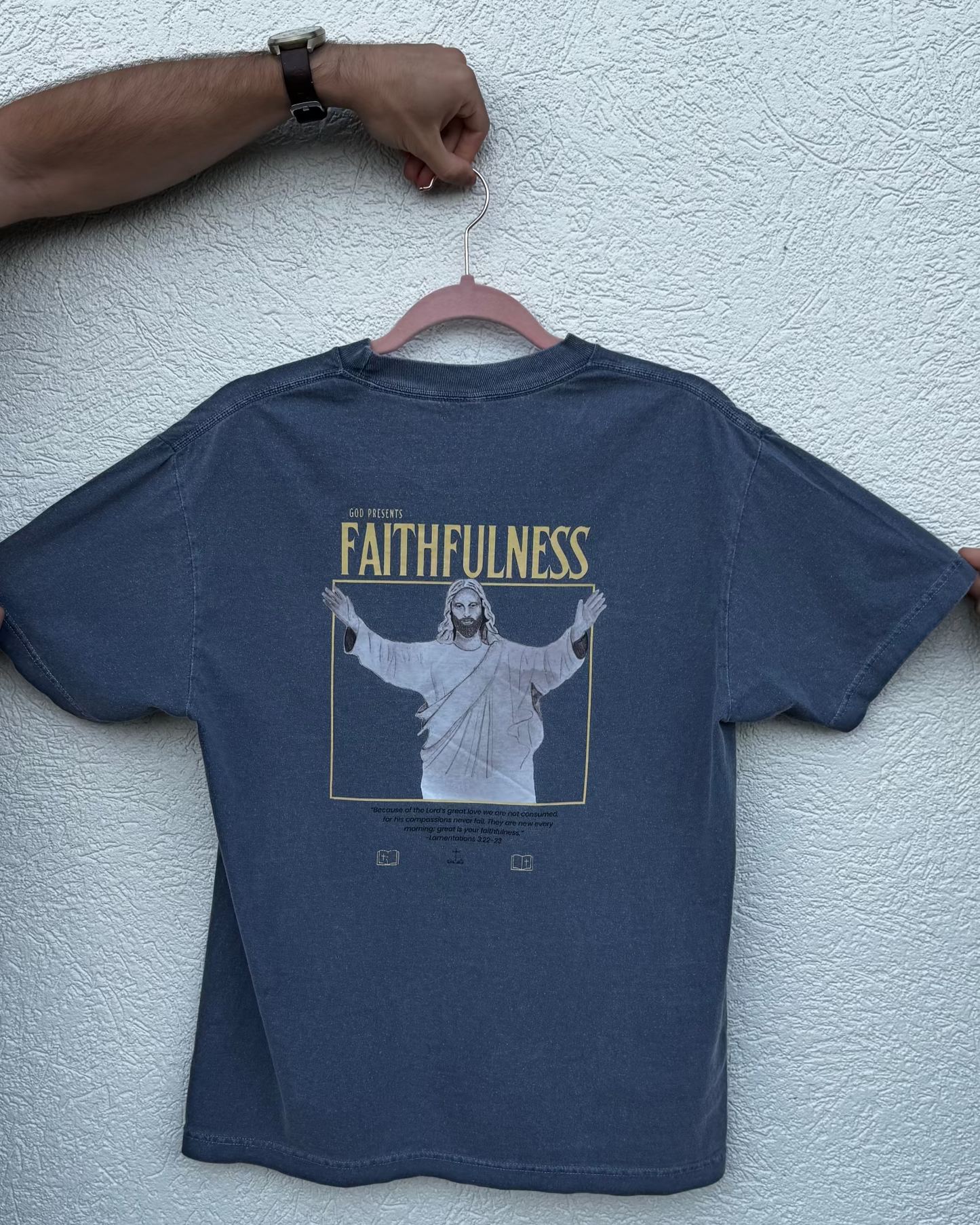 Blue t-shirt with 'Faithfulness' graphic on a hanger against a white wall.