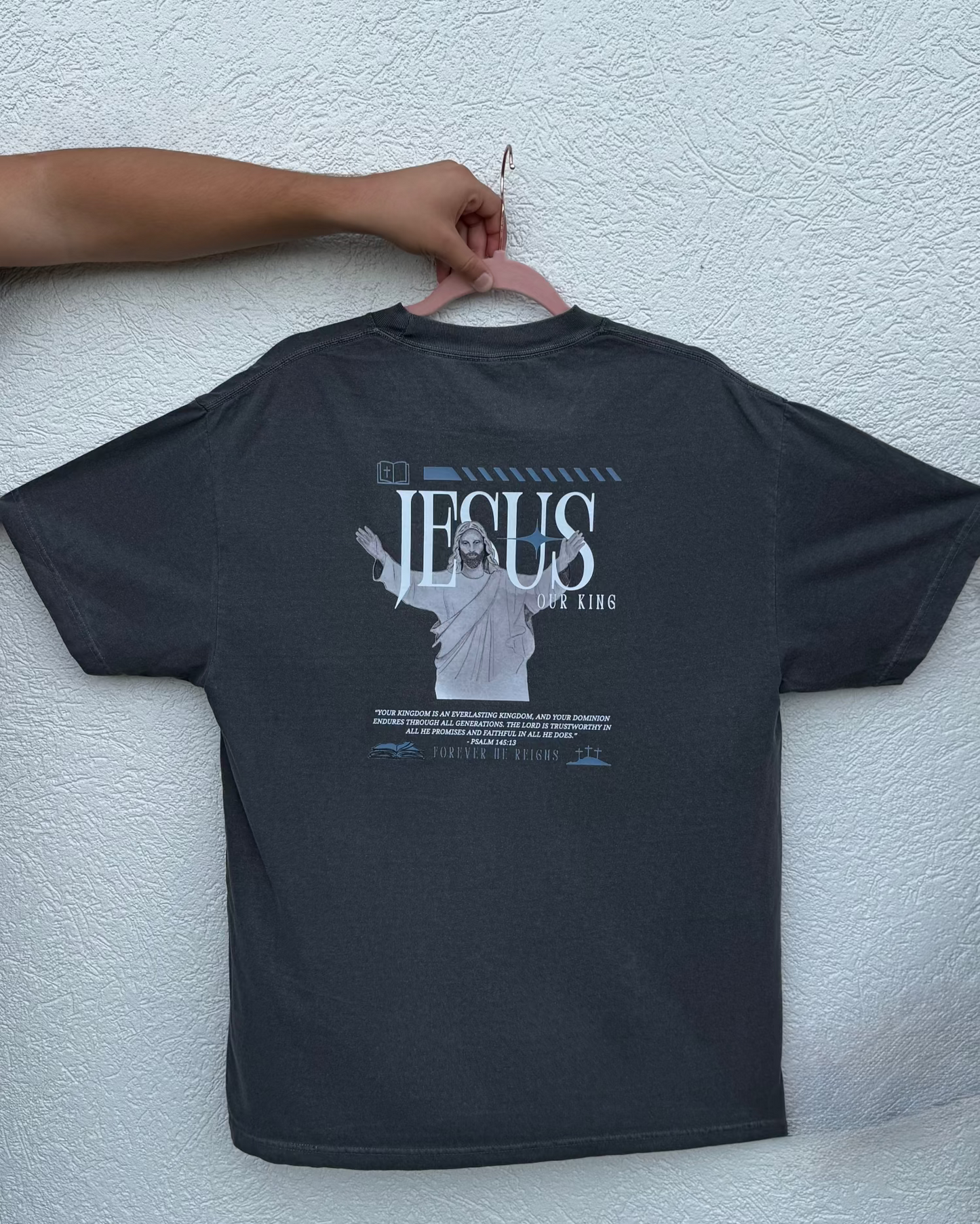 Black t-shirt with a graphic of Jesus on the back, 'Jesus Our King', displayed on a person.