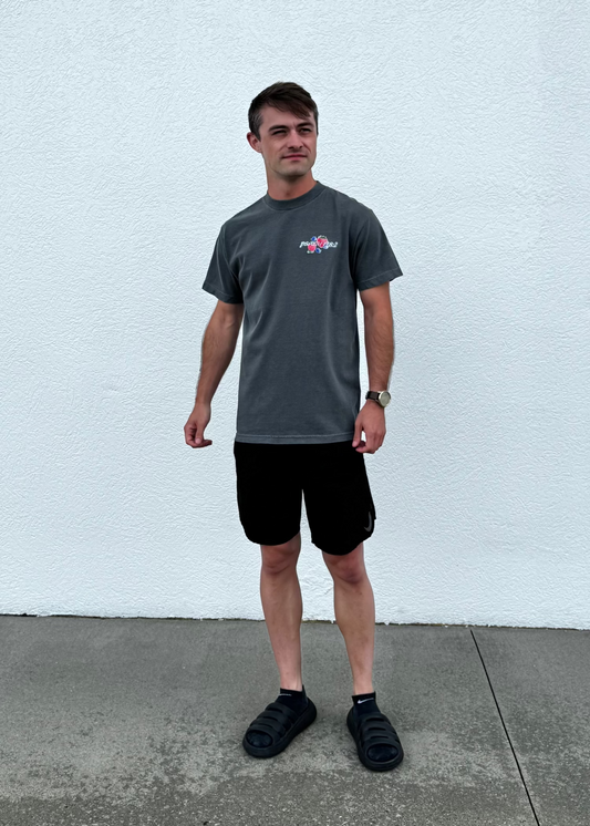 Man wearing a gray t-shirt and black shorts standing against a white wall.